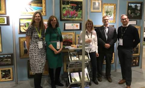 A group of people smile in front of the Cotswolds stand at a show