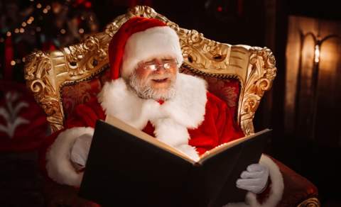 Santa sits in an ornate chair reading a book