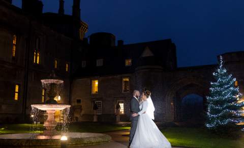 A newlywed couple kiss in the dark next to a fountain and christmas tree at Thornbury Castle