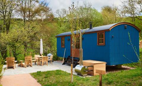 the outside of Shepherds hut painted in blue with garden furniture