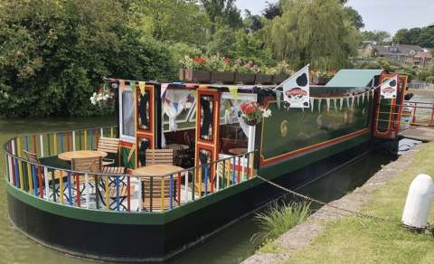 a barge on tiverton canal used as a bar with tables and chairs on a deck