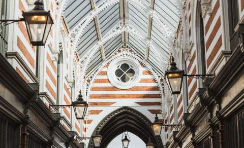 The ceilings of Paragon Arcade with the sun shining through on a clear day. The arches are supported with striped brick and lined with Victorian lamps leading to the shops and cafes below.