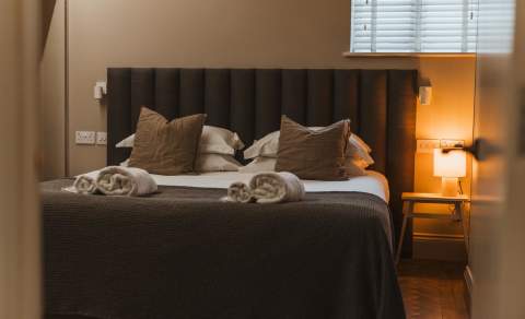 A comfy bed with grey coverings and a light on next to it.