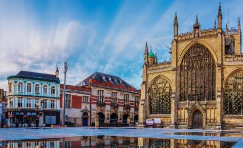 View of Hull Minster and surrounding historic buildings reflected in the mirror pool at Trinity Square on a bright day