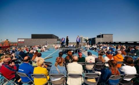 Audience seated outdoors watching Middle Child Theatre’s Biting Point performed on the rooftop of Fruit Market multi-storey car park, Hull, under a clear blue sky.