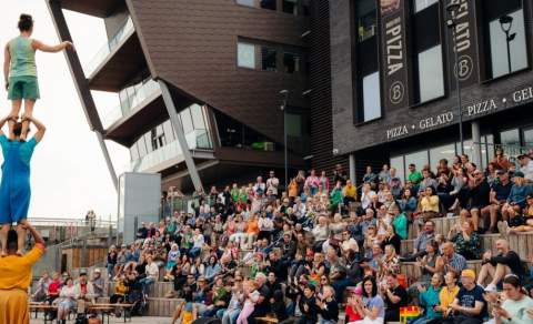 Crowd watching a gymnastics show at Stage@TheDock. Three performers are standing on eachothers shoulders in the foreground with a full audience watching in the ampitheatre seats.