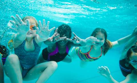 4 barn som svømmer mot kamera under vann