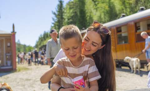Mor og sønn spiser is i sola med gammelt lokmotiv tog i bakgrunnen