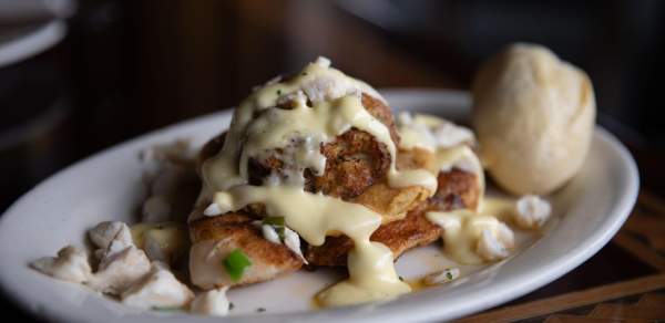 Blackened fish with cream sauce and lump crab meat and a roll on a white oval plate