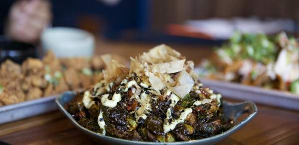 Bowl of wok-fried brussel sprouts sitting on table with other appetizers in the background.