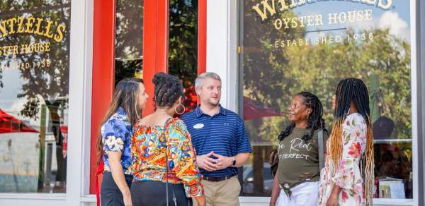 A male tour guide stands outside Wintzell's Oyster House with four female tourists