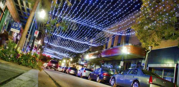 a street full of cars outside of restaurants with strings of lights overhead