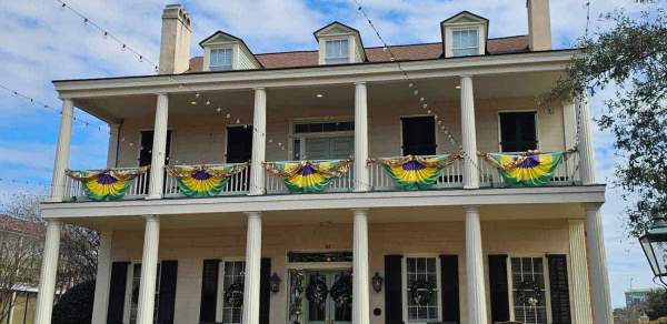 Two story white house with columns and Mardi Gras decorations