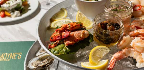 A tower of plates containing shrimp, oysters and seafood on ice with lemon and two glasses of white wine