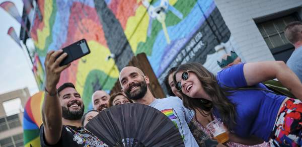 group of people taking a selfie in front of a rainbow mural