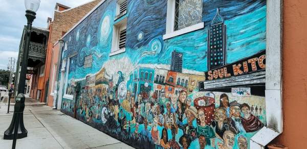 Swirly blue mural with the city behind a crowd of people