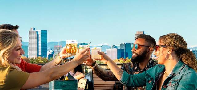 Four people smile as they toast on a rooftop patio in Denver with mountains in the background