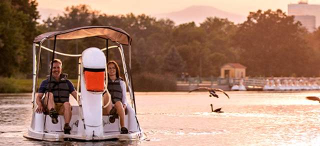Two people pedaling on a swan boat at sunset in City Park