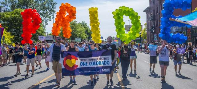 A group of people holding a sign march in the Denver PrideFest parade
