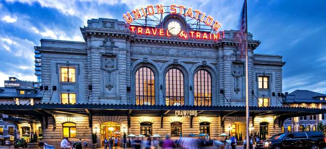 Denver Union Station glows at night with people milling around in front
