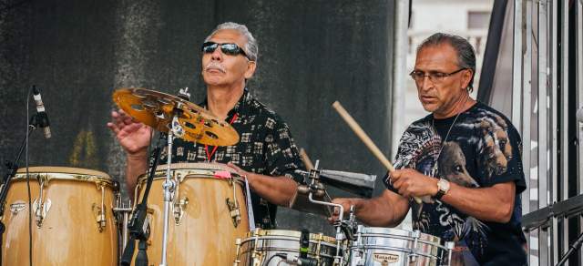 Two people play the drums during a performance in Denver
