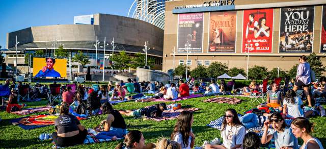 People gather on a green lawn watching a movie outside of the Arts Complex