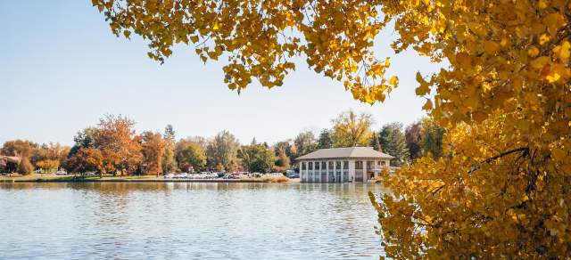 The pavilion at Washington Park in Denver is seen from across the lake, framed by golden leaves