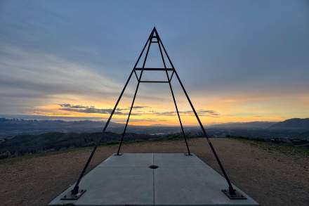 Steel pyramid structure on top of a mountain with sunset and clouds in the background