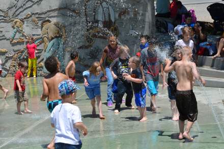 Children playing in a splash pad fountain with a background of miners and pioneer wagons on the wall