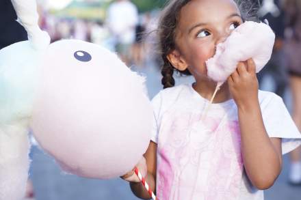 Girl holding a cotton candy animal and stuffing a big cloud of cotton candy into her mouth