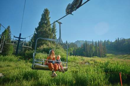 Mother and child sitting on lift chair with green mountain and trees