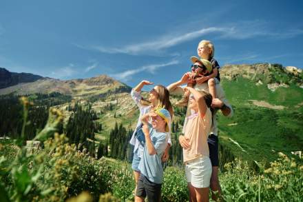 Family on a mountain trail all shading their eyes and looking at something in the distance with mountains in the background