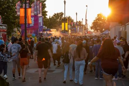 A crowd of people walking down the area between fair booths advertising fair food