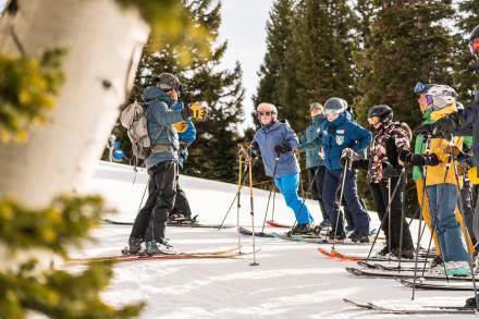 Looking past an aspen tree at a group of skiers listening to another skier who is speaking to them