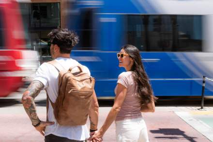 Two people holding hands waiting to cross the street with a Trax light rail train going by in the middle of the street