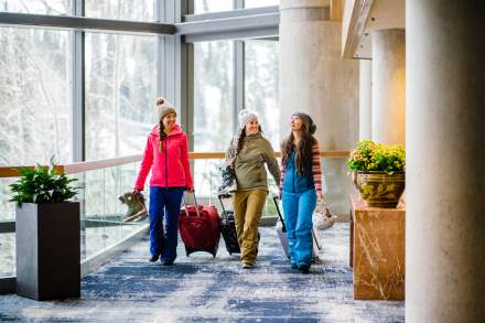 3 women in ski gear pulling suitcases in the atrium area of the Cliff Lodge
