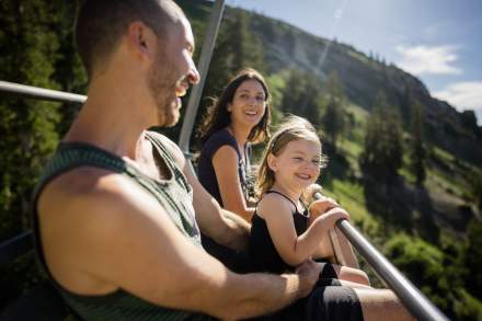 Man woman and child on a ski lift with summer mountains and sunshine