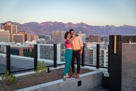 Couple standing and taking a selfie on the roof at Van Ryder with Salt Lake City Skyline and wasatch mountains in the background