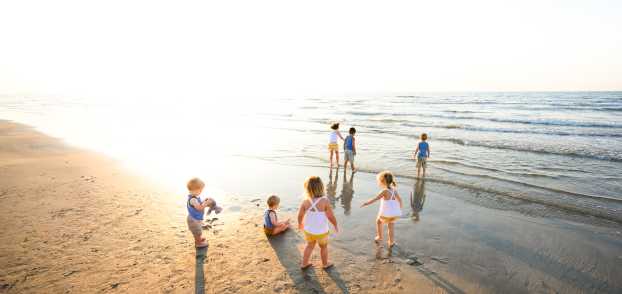 A group of seven kids of various ages play on the beach in coordinating yellow and blue outfits