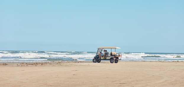 A golf cart sits on the beach in the distance with waves crashing behind.