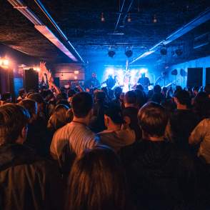 crowd enjoying a band on a lighted stage in a dark concert venue