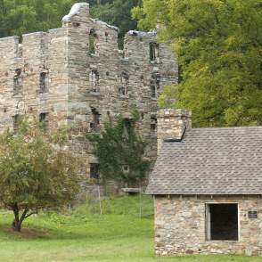 A 4-story cobblestone building with a missing roof is in the background, in the front is a small cobblestone cabin