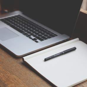 Laptop computer with notebook and pen laying beside it
