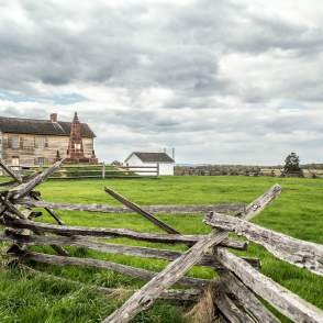 A battlefield with a wooden fence and a historic building in the background