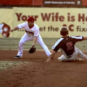 Two baseball players, one is sliding into base and the other is trying to catch a ball to get an "out".