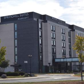 a hotel with black and grey bricks with a driveway and small trees in the front
