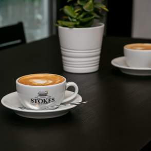 Stokes coffee mug with coffee on table with plant in background