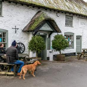 Table of men and a dog sat outside a thatched pub in winter