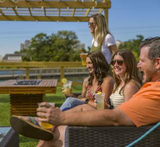 Group of friends relaxing with drinks and appetizers on a sunny outdoor patio in North Myrtle Beach, South Carolina, enjoying casual coastal dining and vibrant social atmosphere under a pergola.