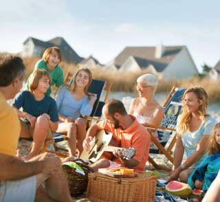 Friends having an oceanfront picnic with beach houses in the background.